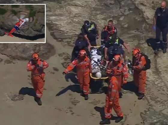 An image collage containing 2 images, Image 1 shows Emergency personnel carrying an injured woman on a stretcher over rocky terrain, Image 2 shows Aerial view of a red and white helicopter above a sandy beach and rocky cliff