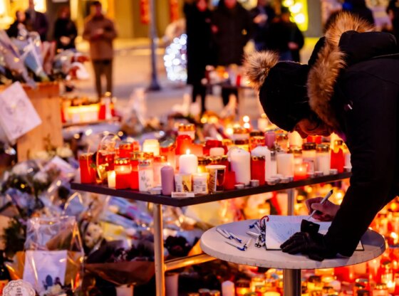 An image collage containing 1 images, Image 1 shows A person writes a message in a condolence book for victims of a New Year's Day fire at a Swiss ski resort, surrounded by lit candles