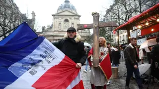 A man holds a wooden cross that reads Pray for Quentin and another a flag during a demonstration to honor Quentin, the 23-year-old student murdered in Lyon.