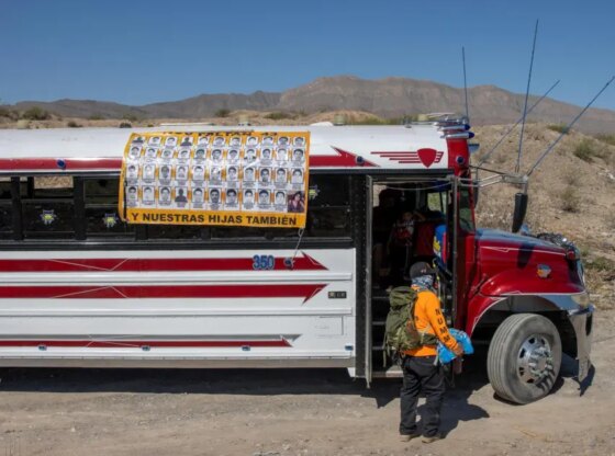 A member of the Armadillos International search group unloads bottles of water for volunteers, next to a bus covered with a tarp that shows the faces of Esmeralda and the 43 missing students from Ayotzinapa.